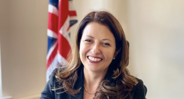 Joy at her desk with UK flag behind 